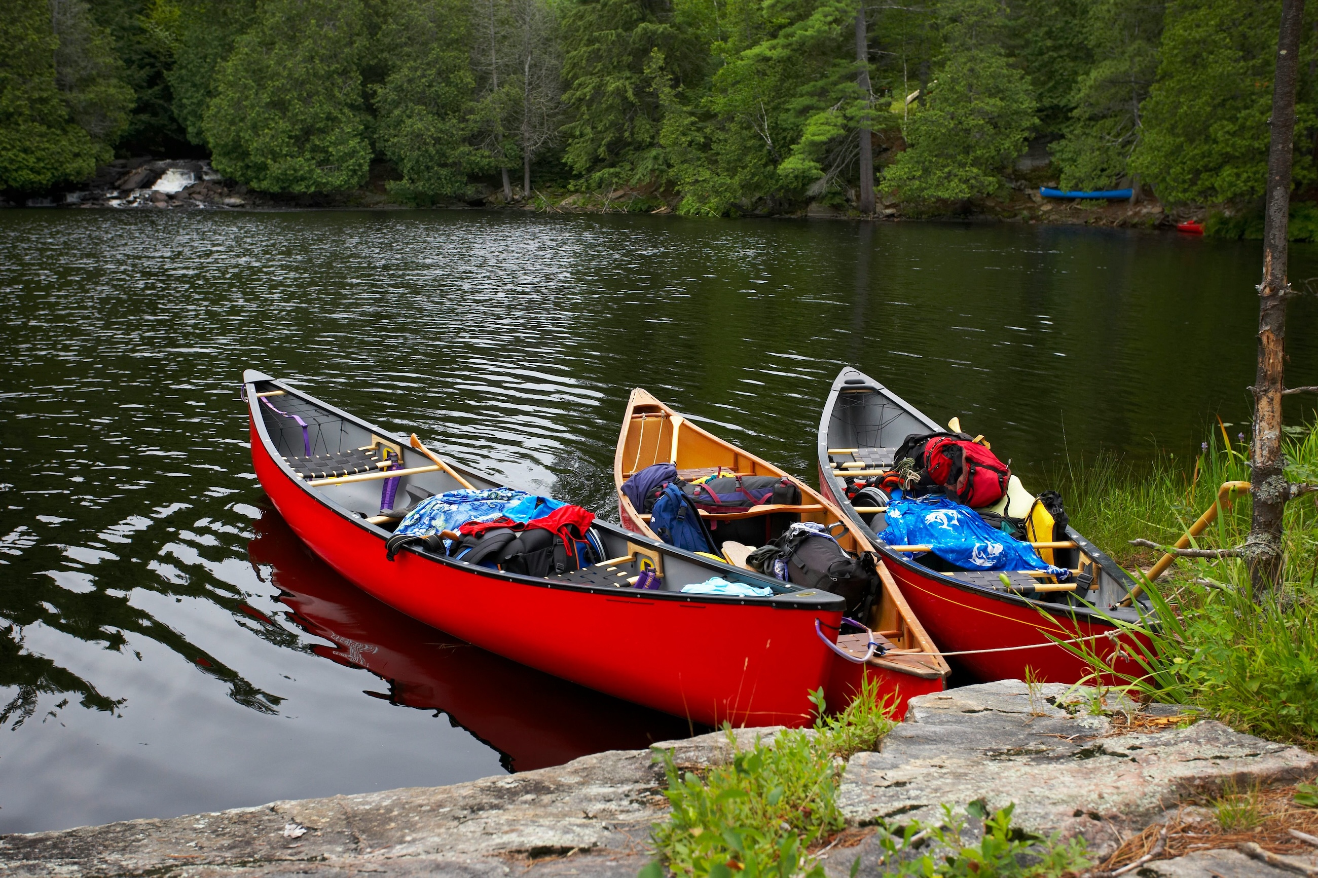 Three loaded canoes pulled up on a rock shore at a forest lake
