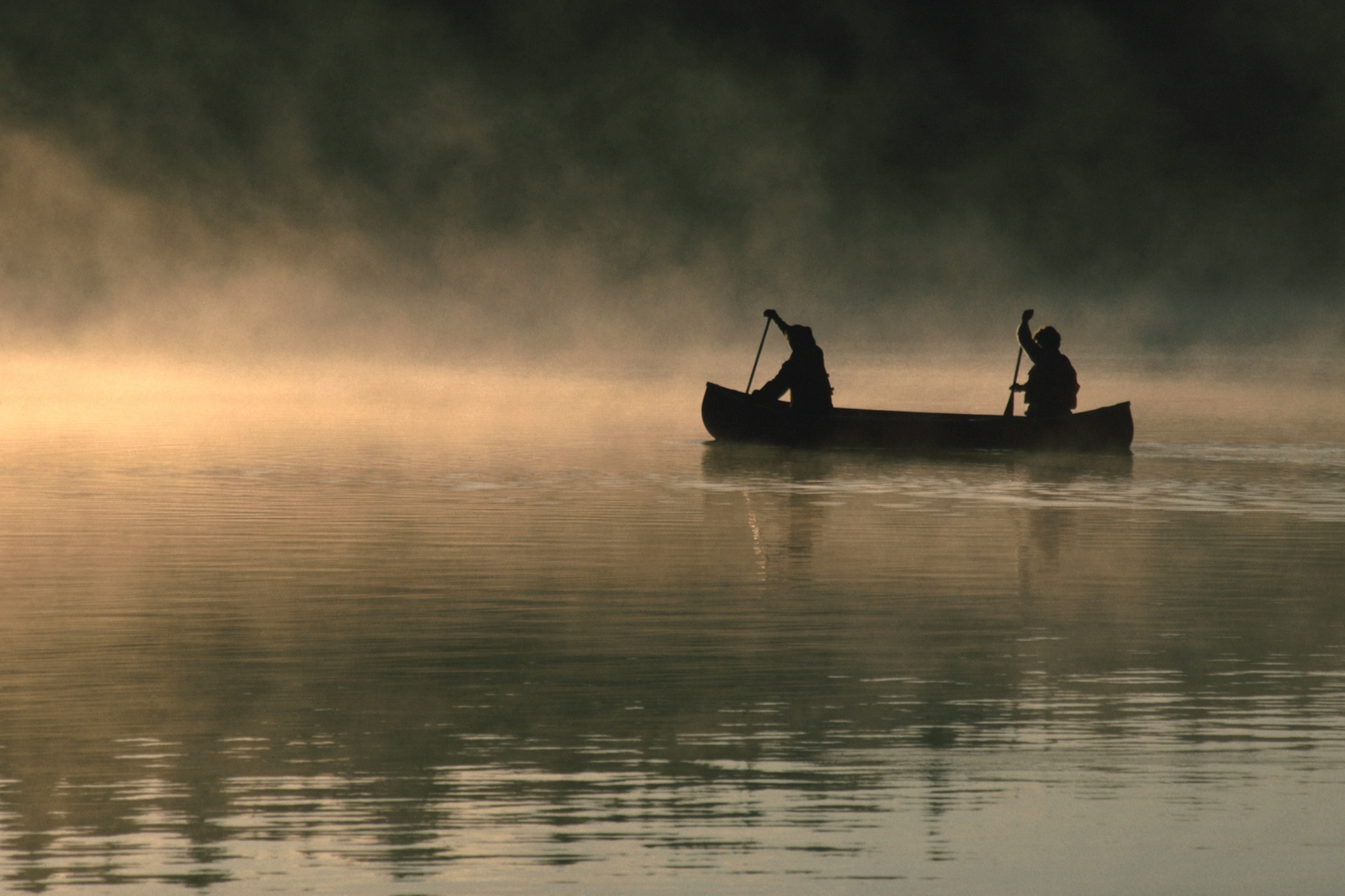 Two paddlers crossing a misty lake at dawn in a silhouetted canoe