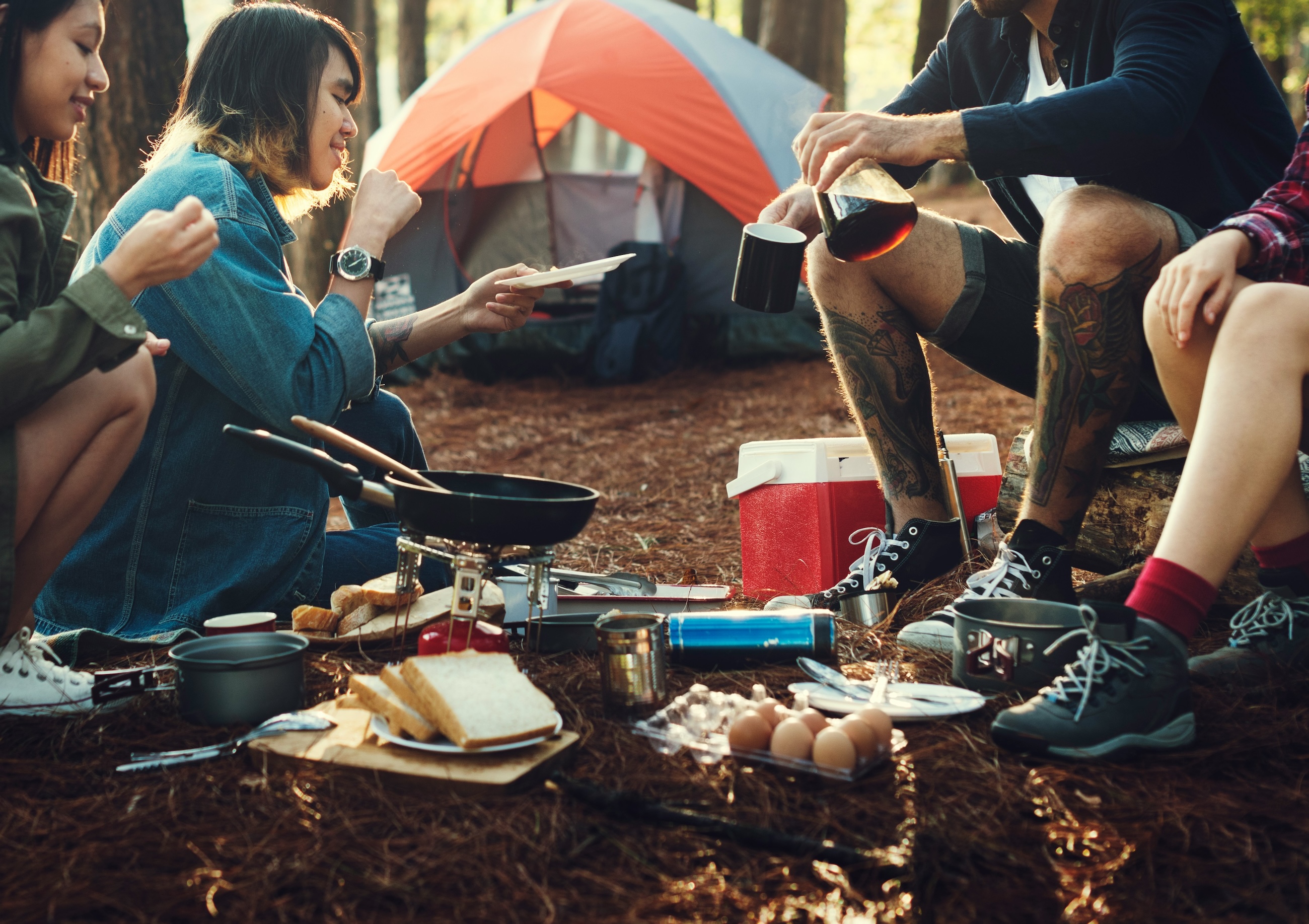 Camp cooking gear, food and a stove spread out at a forest campsite