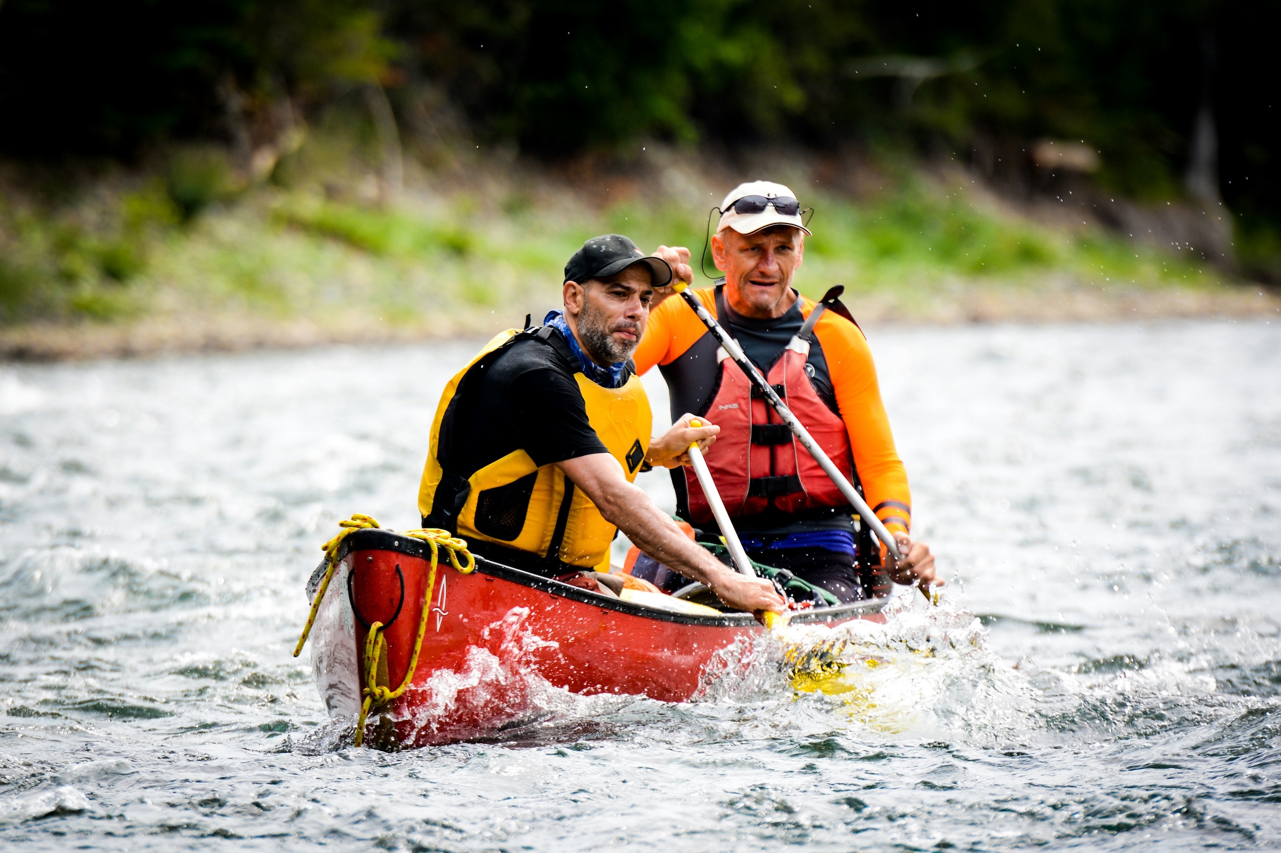 Two paddlers running a whitewater river in a loaded red canoe